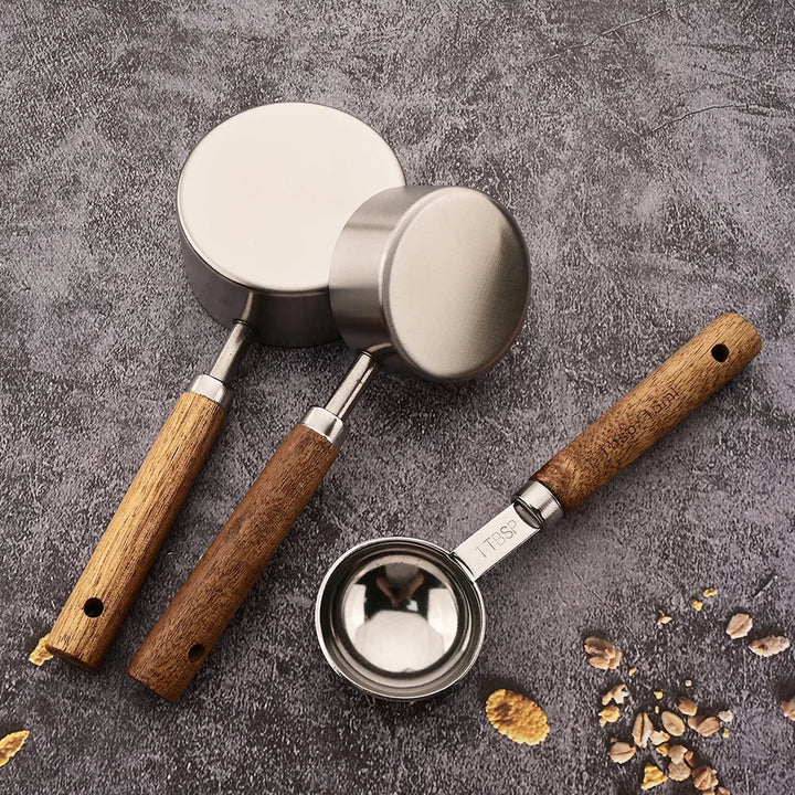 Three metal measuring cups with wooden handles on a gray surface.