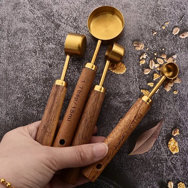 Set of wooden measuring spoons with gold accents held by a hand on a textured surface.