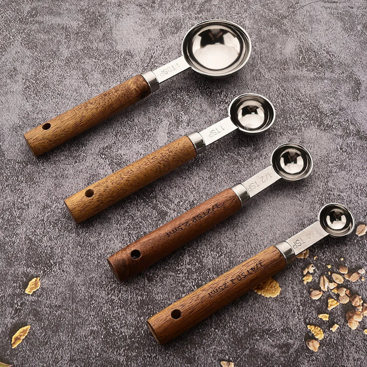 Set of four wooden-handled metal measuring spoons on a textured surface with scattered grains.