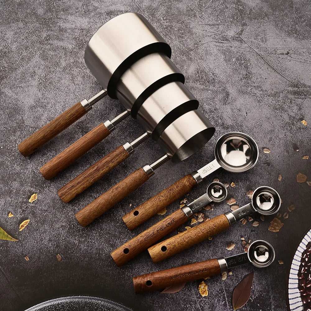 Set of coffee tools including a silver tamper and multiple espresso scoops with wooden handles on a dark surface.