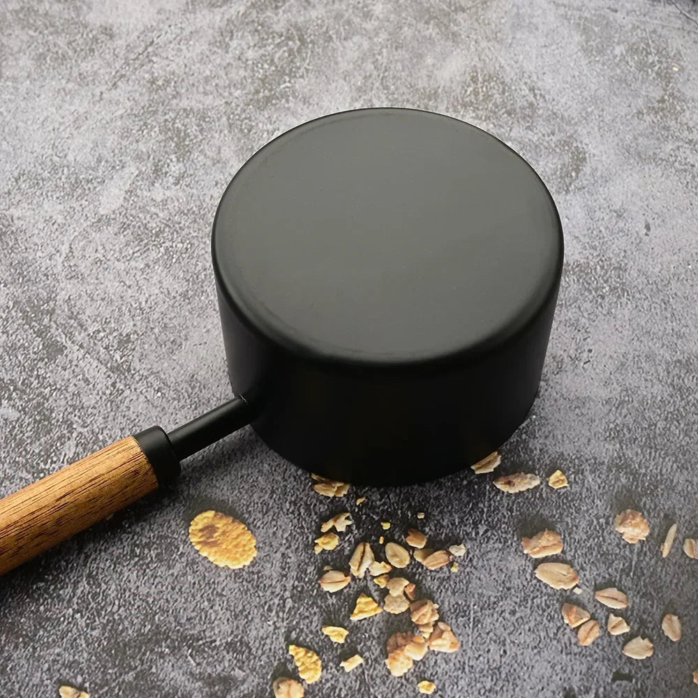 Black pot with wooden handle on a gray surface with small stones and pebbles.