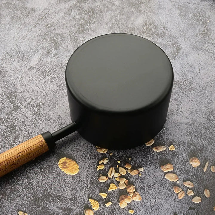 Black pot with wooden handle on a gray surface with small stones and pebbles.
