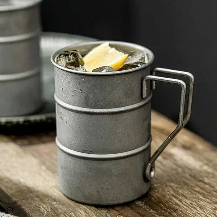 Metallic mug with a drink and lemon wedge on a wooden surface