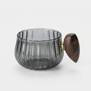 A ribbed translucent smoky gray glass cup with a dark brown wooden lid and a small gold metal accent ring, shown on a light gray background.
