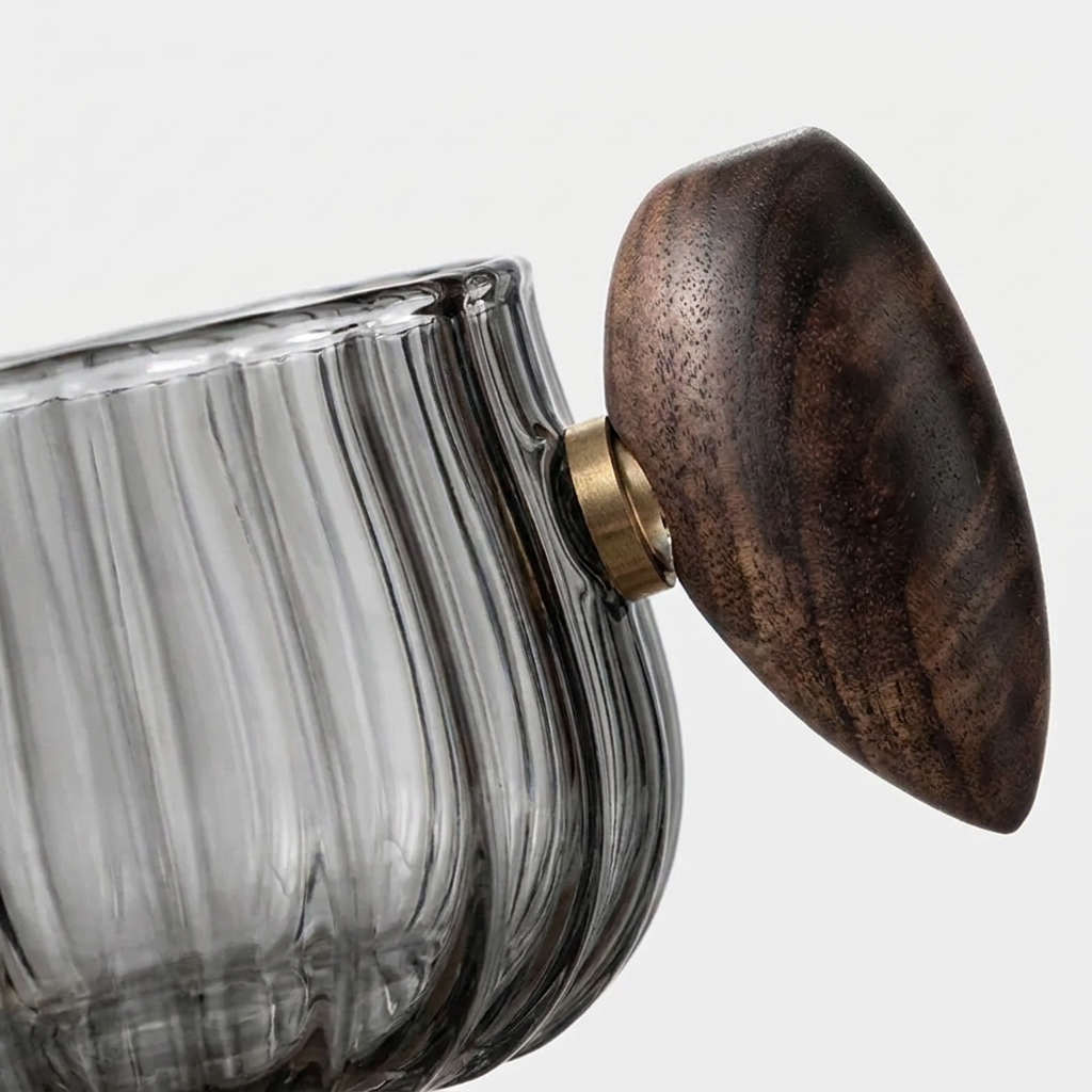 Close-up of a ribbed clear glass container with a dark brown wooden lid and a brass metal knob, set against a light gray background.