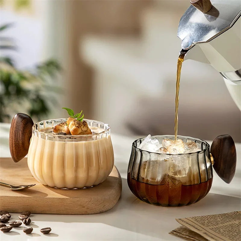 Two glasses of creamy drinks with a pitcher pouring liquid, set on a wooden board.