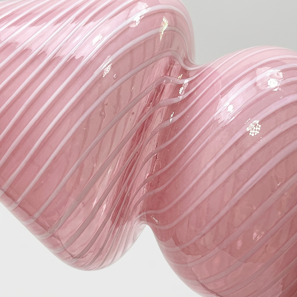 A close-up of a glossy pink sculptural vase with a wavy, ribbed form and smooth translucent finish on a light gray background.