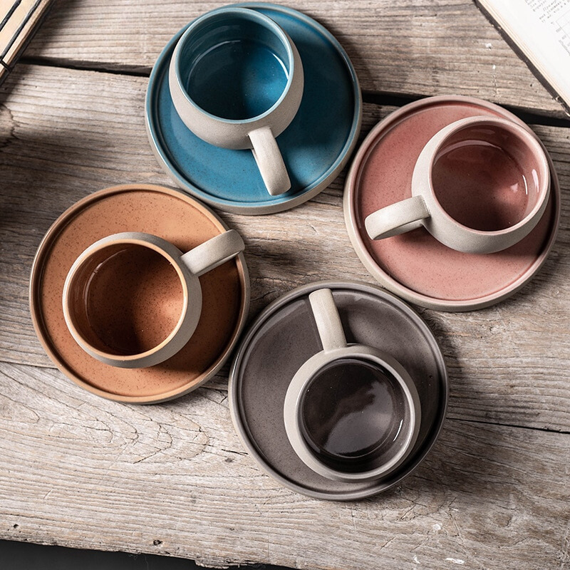 Set of ceramic mugs and saucers in various colors on a wooden surface