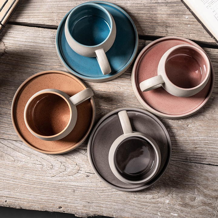 Set of ceramic mugs and saucers in various colors on a wooden surface
