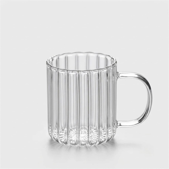 A clear ribbed glass mug with a flared rim and a curved handle, shown on a light gray background.