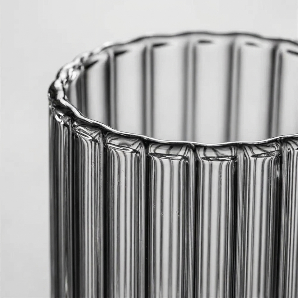 Close-up of a ribbed clear glass cup or vase with a scalloped rim, shown against a light gray background.