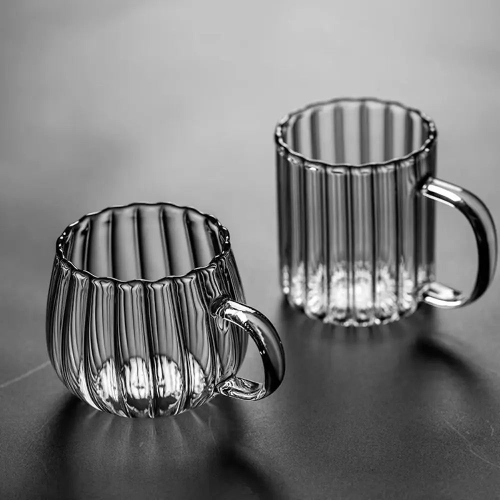 Two ribbed glass mugs on a reflective surface with a gray background