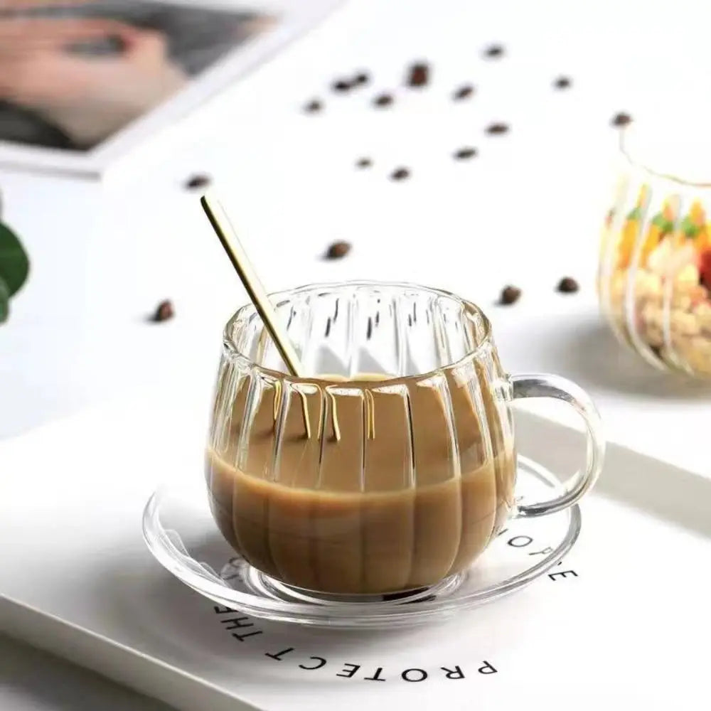 Glass mug with coffee and a spoon on a white surface with coffee beans scattered around.