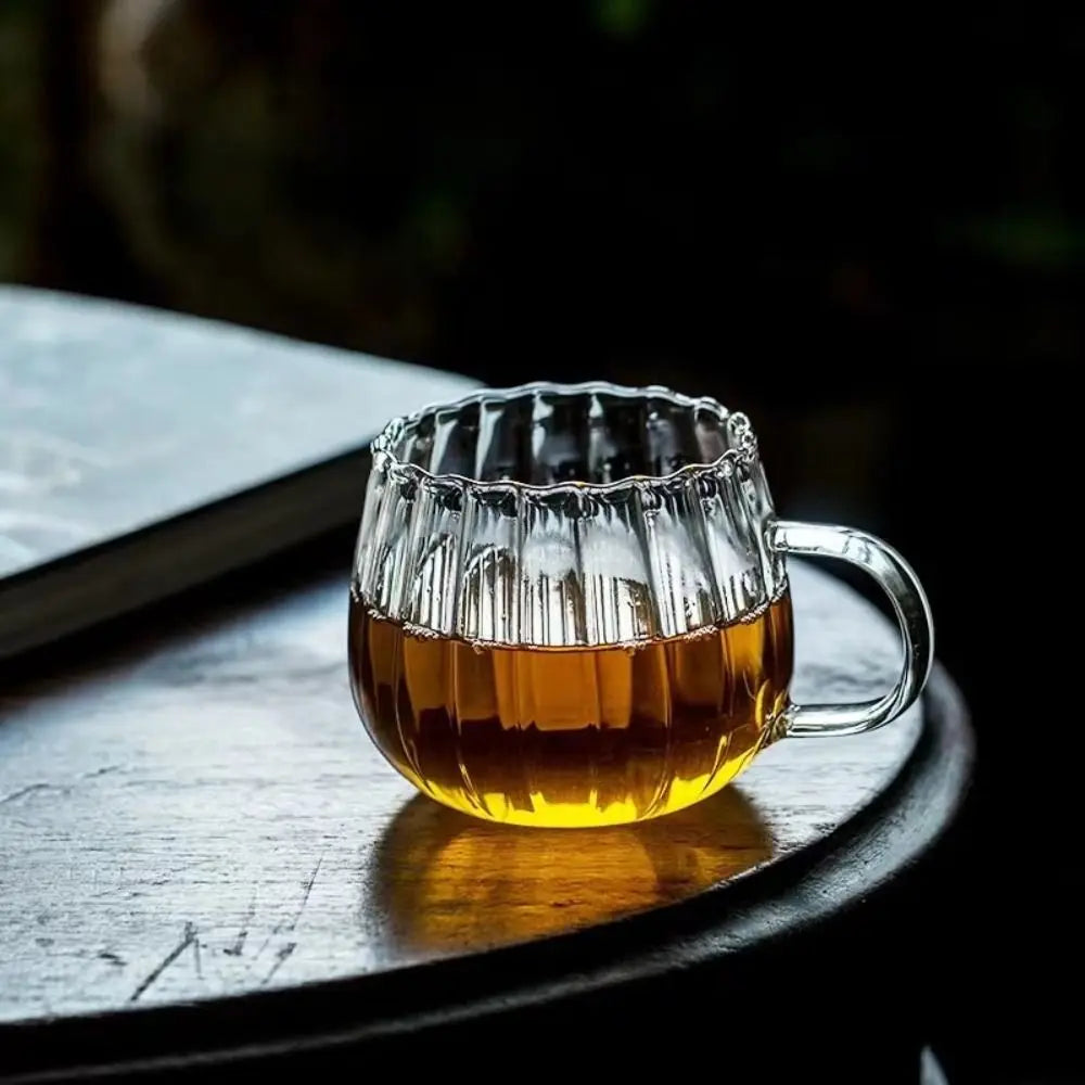 Clear glass mug with textured rim filled with amber liquid on a wooden surface.