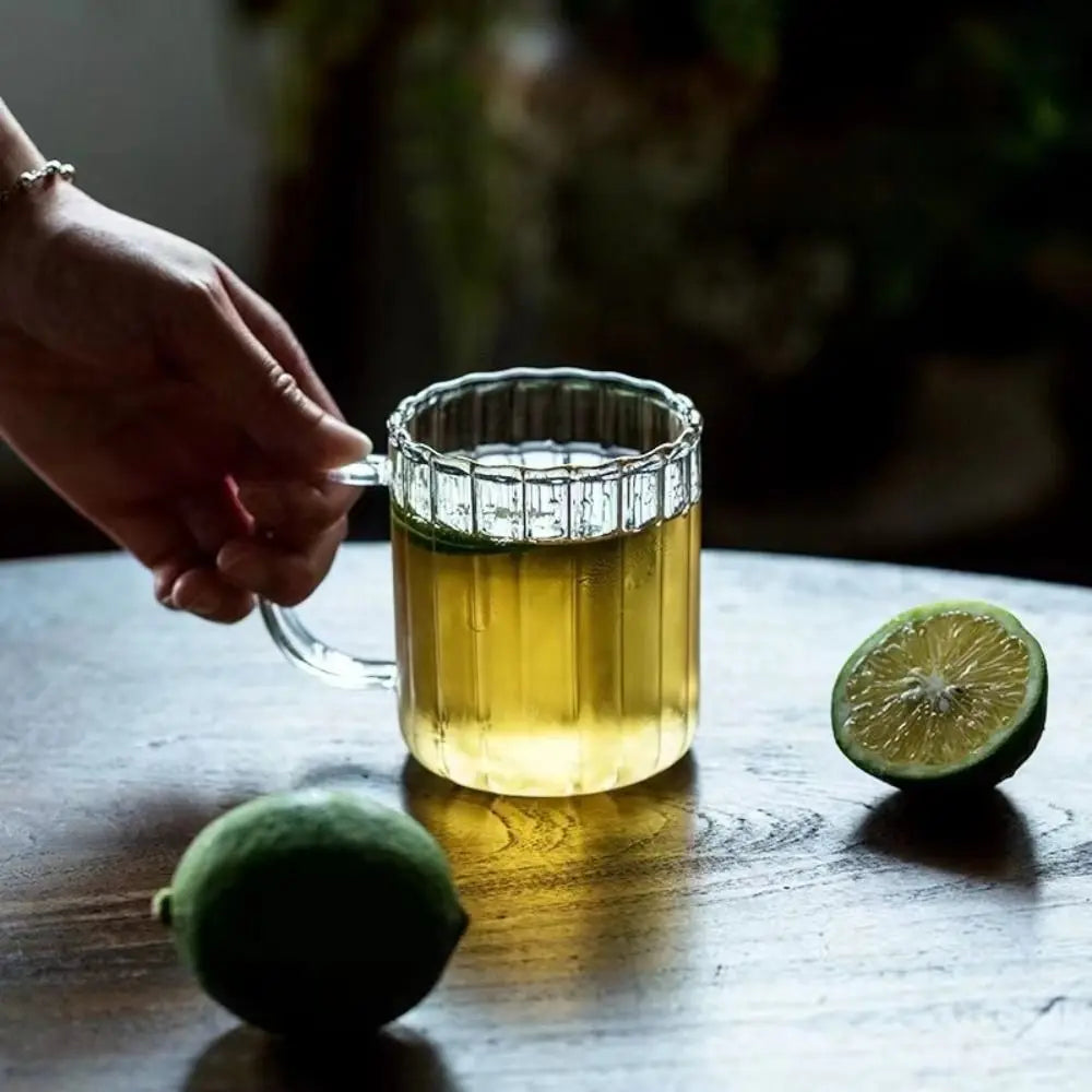 Clear glass mug with green tea on a wooden table with limes, blurred background