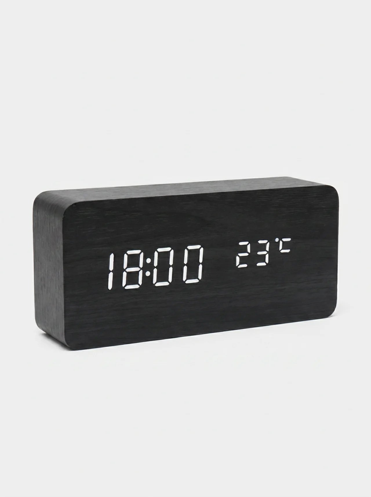 A modern rectangular digital clock with a dark wood grain finish and white LED display showing 18:00 and 23°C, set against a light gray background.