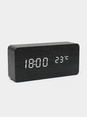 A modern rectangular digital clock with a dark wood grain finish and white LED display showing 18:00 and 23°C, set against a light gray background.