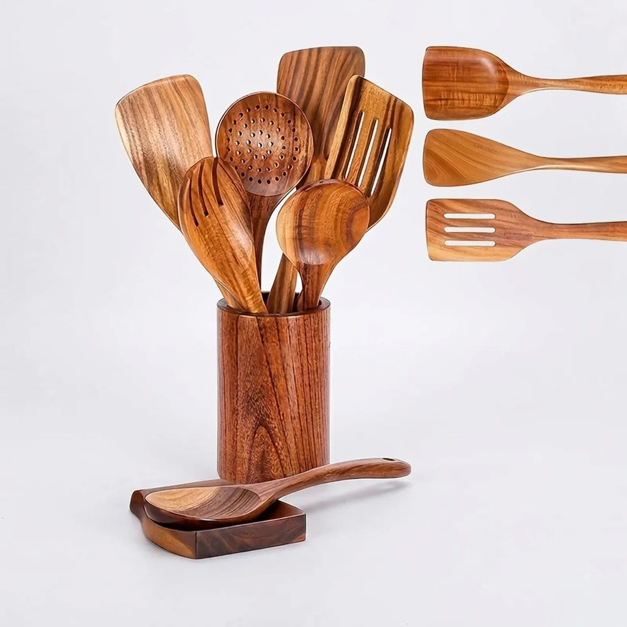 A set of wooden kitchen utensils with a warm medium-brown finish and visible wood grain, including a slotted spoon, spatulas, and a ladle, displayed in a matching wooden holder with one utensil resting on a small stand. Three additional utensils are shown floating on the right against a clean white background.