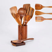 A set of wooden kitchen utensils with a warm medium-brown finish and visible wood grain, including a slotted spoon, spatulas, and a ladle, displayed in a matching wooden holder with one utensil resting on a small stand. Three additional utensils are shown floating on the right against a clean white background.