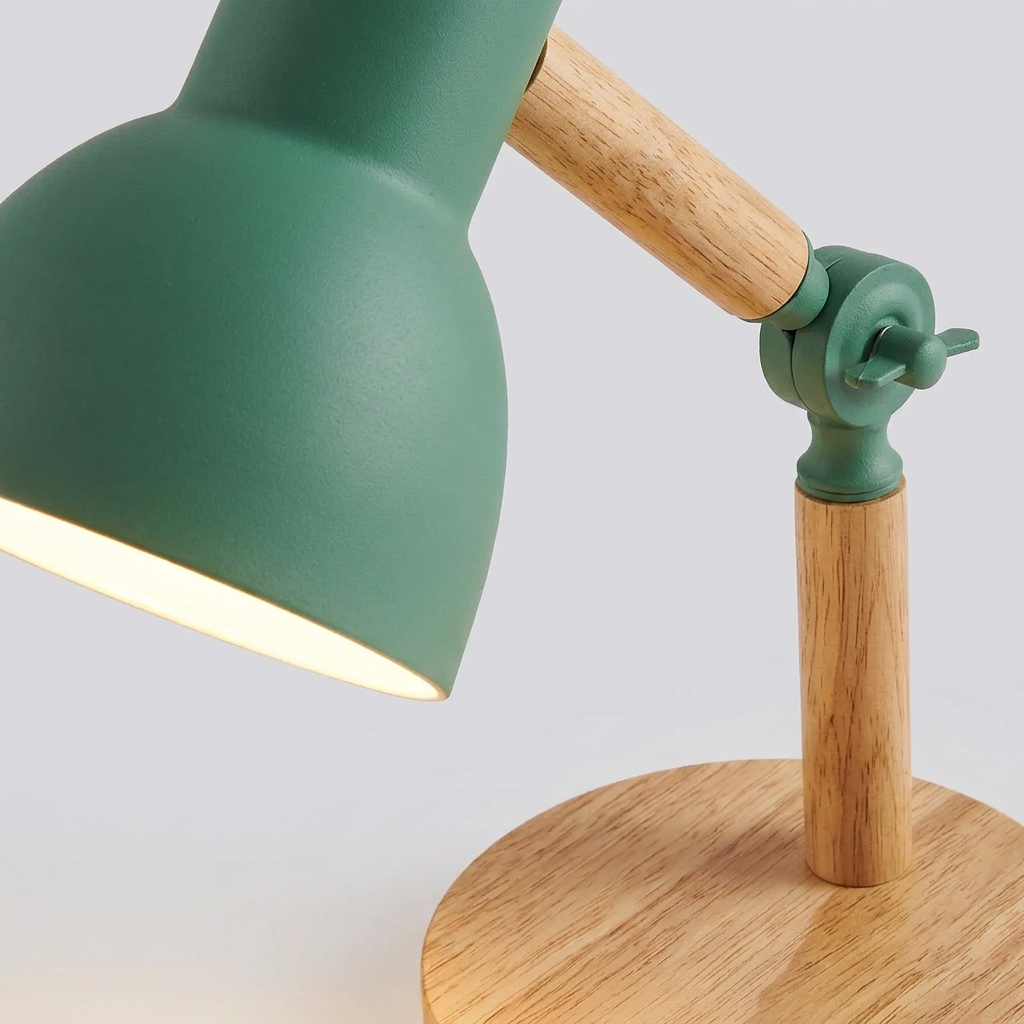 A close-up of a modern desk lamp with a matte green metal shade and adjustable wooden arm on a round wooden base, shown lit against a light gray background.